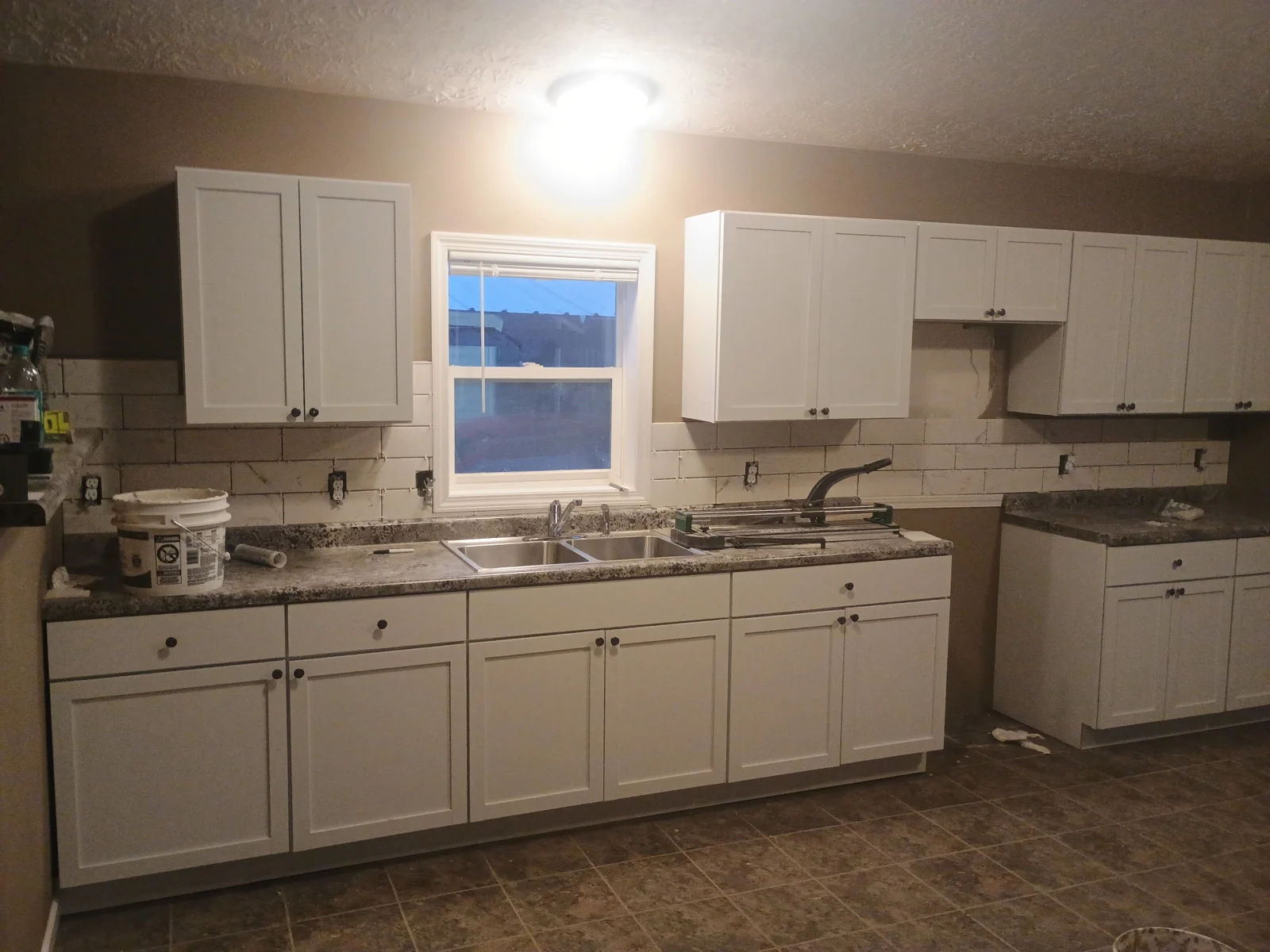 Cabinet installation, backsplash, and window trim in a mobile-home kitchen.